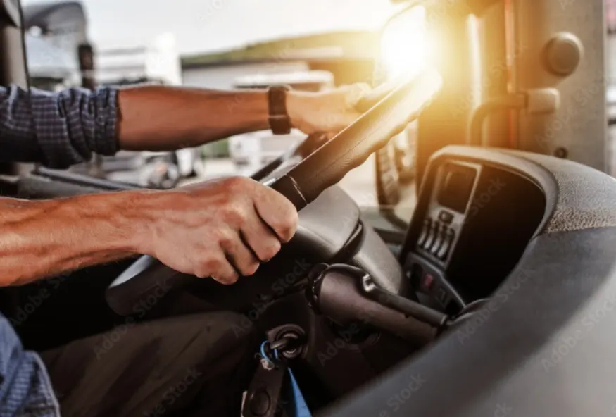 Close-up of a driver holding the steering wheel of a truck, with sunlight entering through the vehicle's window.